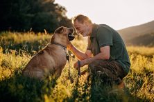 A man shows affection to his dog in a field during a walk.
