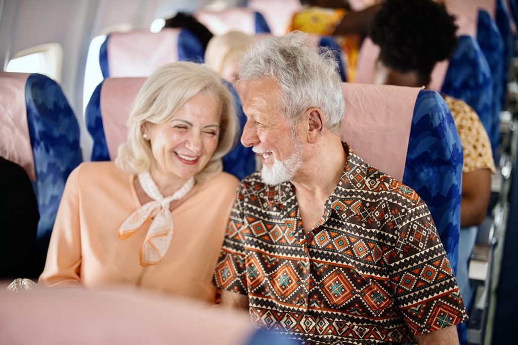 An elderly couple laugh while on an airplane.