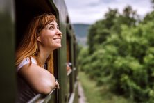 A woman smiles as she looks at a scenic view of trees through a train.