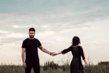An unhappy man and woman stand in a field barely locking fingers. Meant to represent breaking up.