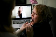 A mother looks at the back of their child&rsquo;s throat with the doctor on the laptop during a telemedicine visit.