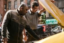 Two men tend to a car broken down on a street.