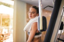 A young woman stands in a fitness center setting near a piece of workout equipment.