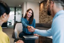 A woman shakes hands with two people during a job interview.