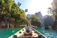 A woman celebrates her visit to a tropical location while sitting on the bow of a boat.
