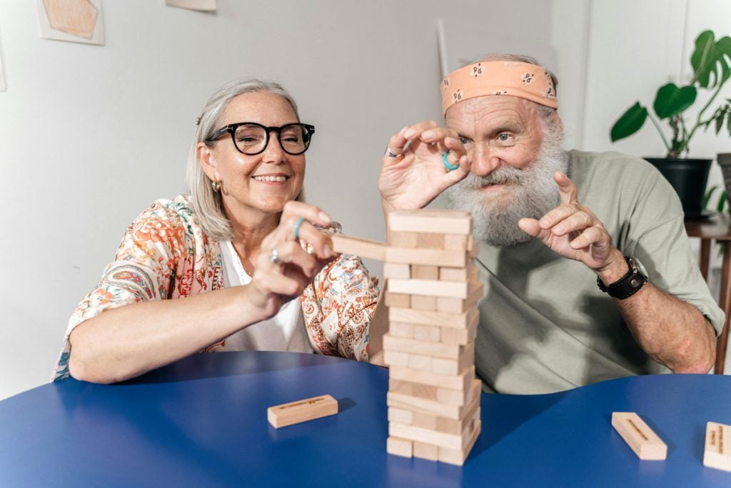 Two retired people play Jenga in their living room.
