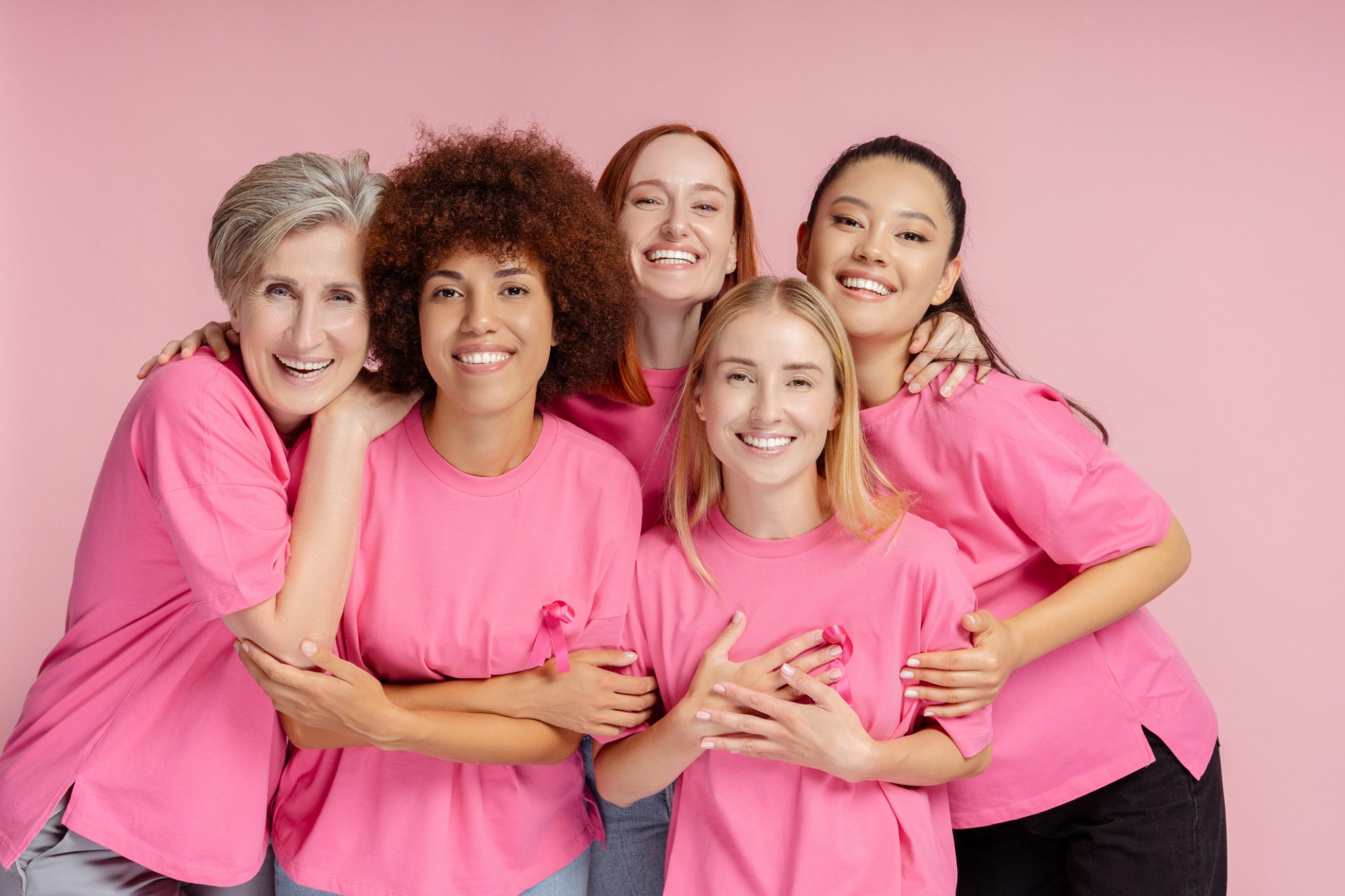 Smiling women with susan g komen. wearing t shirts with pink ribbon isolated on pink background. Breast cancer
