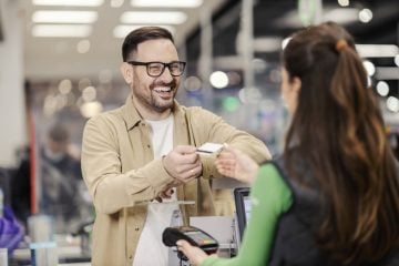 A smiling man giving credit card to a cashier and paying for groceries in supermarket.