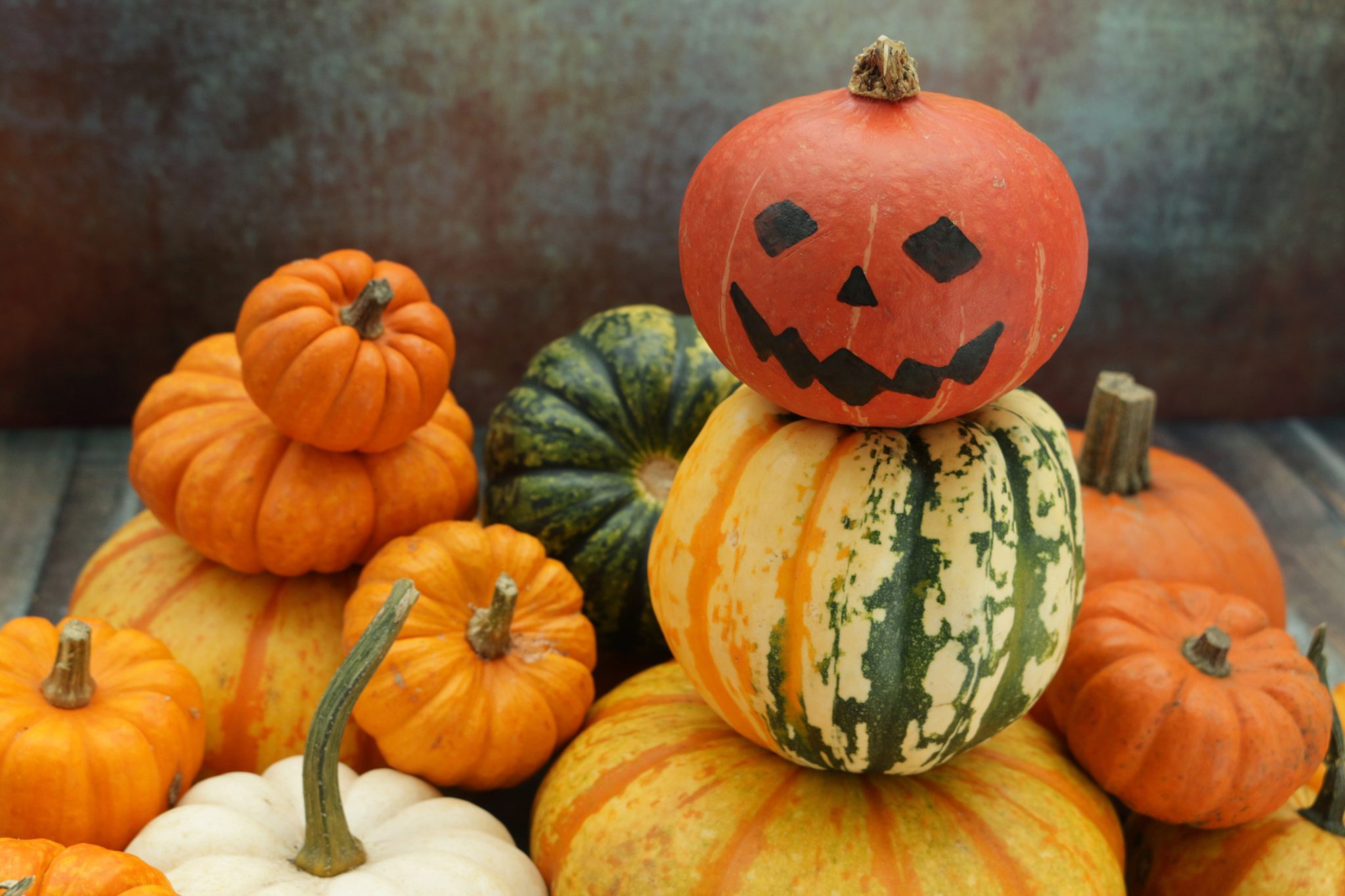 Image of pumpkin snowman surrounded by pile of orange and green gourds and pumpkins