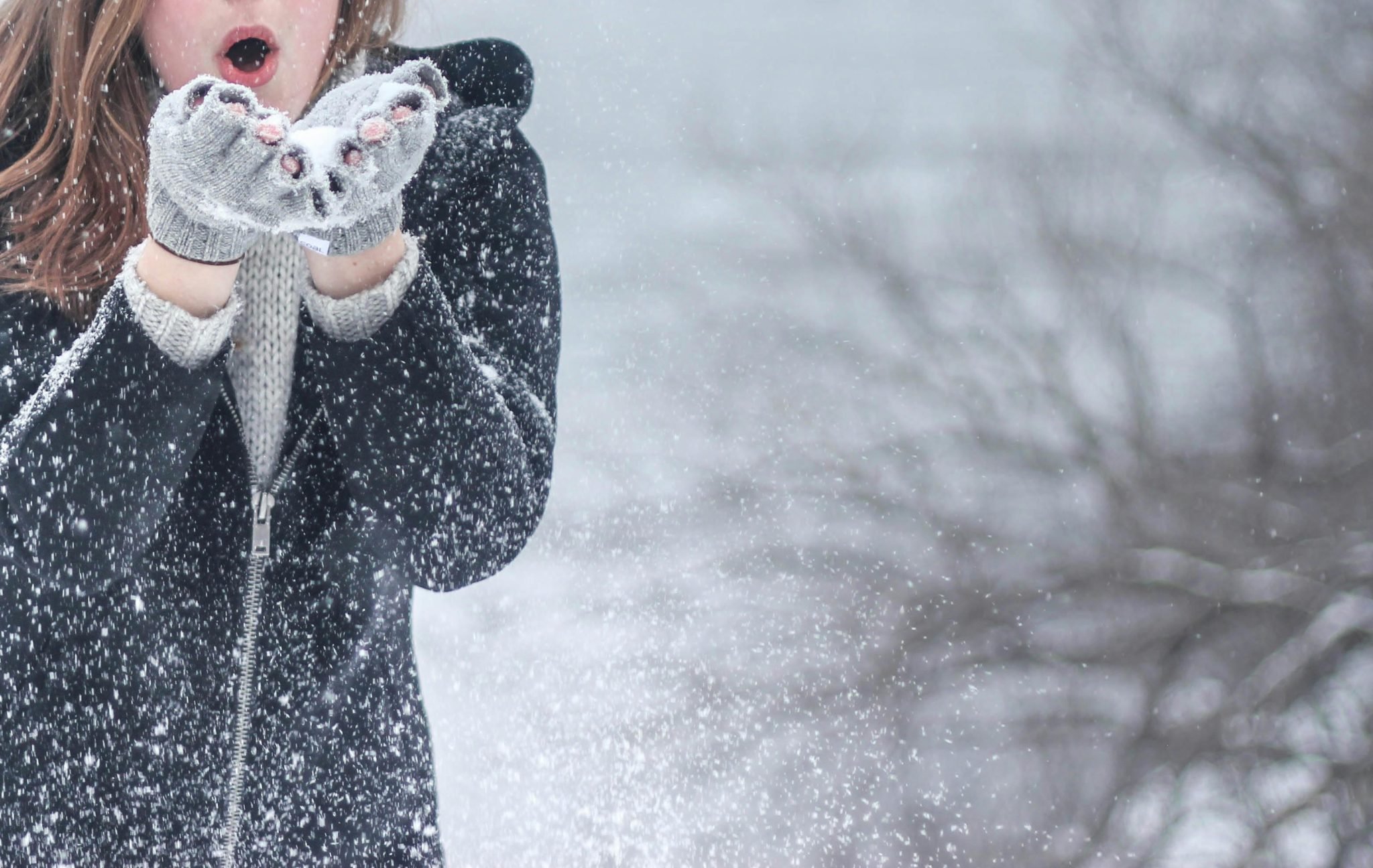 A woman blows snow out of her hands. 
