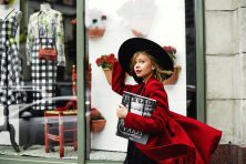 A woman in a red coat and black hat walks down a street with stores to shop at.