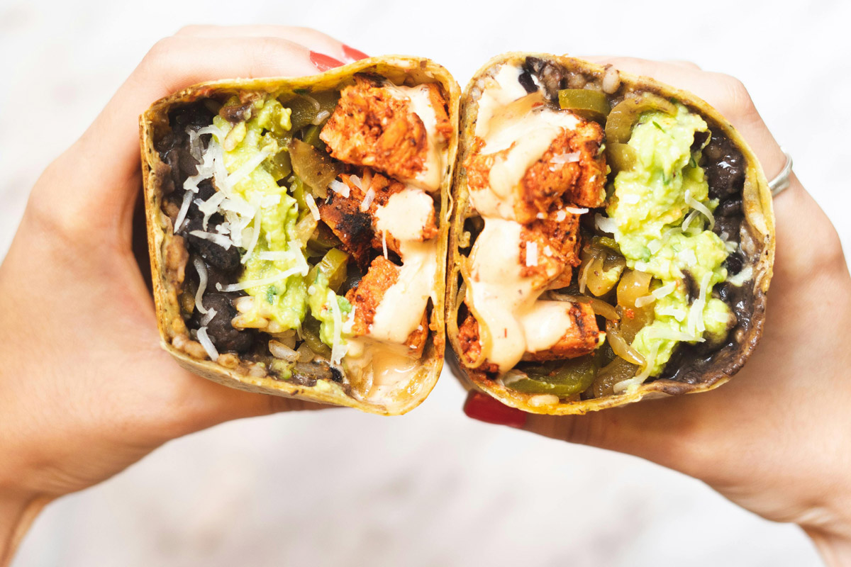 A woman holds a burrito cut open.