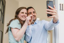 A young couple take a selfie with their phone in the doorway after purchasing a new home.