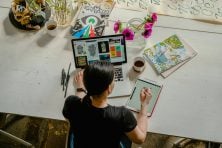 A graphic designer sits at a desk and uses a tablet and laptop to illustrate logos.