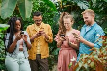 Four young adults standing in a garden, look at their smartphones.