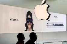 Two people are silhouetted against an apple sign and an advertisement for their VisionPro.