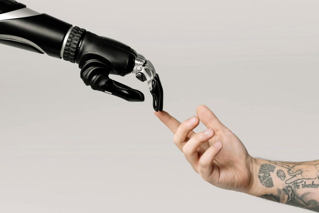 A robot hand touches a human hand covered in tattoos.