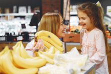 A woman and child smile at each other as they pick out organic bananas at the grocery store.