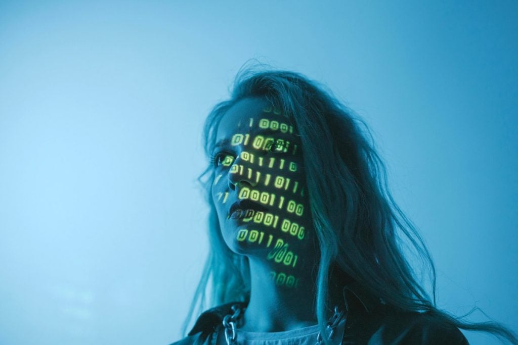 A woman looks up with computer data reflected on her face.