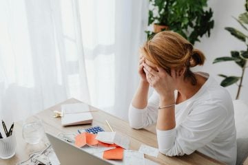 A woman looks at a desk looking stressed.