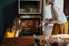 A young girl and young woman look at something baking in an oven.