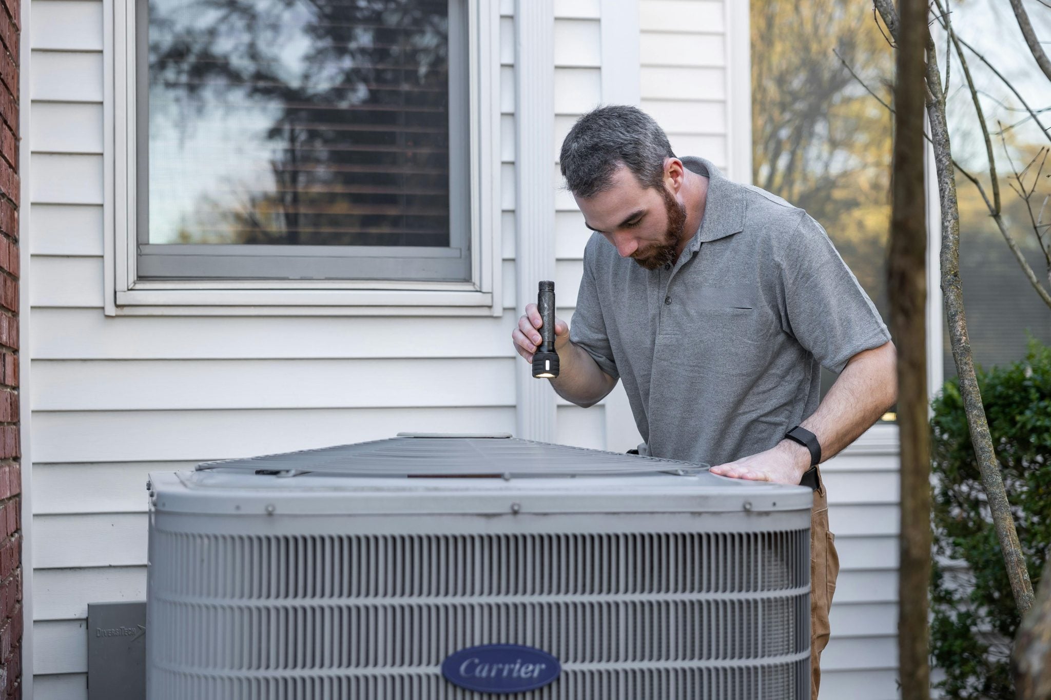 A man looks at an air-conditioning unit with a flashlight. 