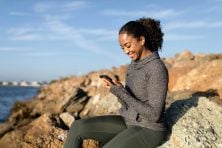 A woman sits on a rock on top of an elevated. view while looking at her phone.