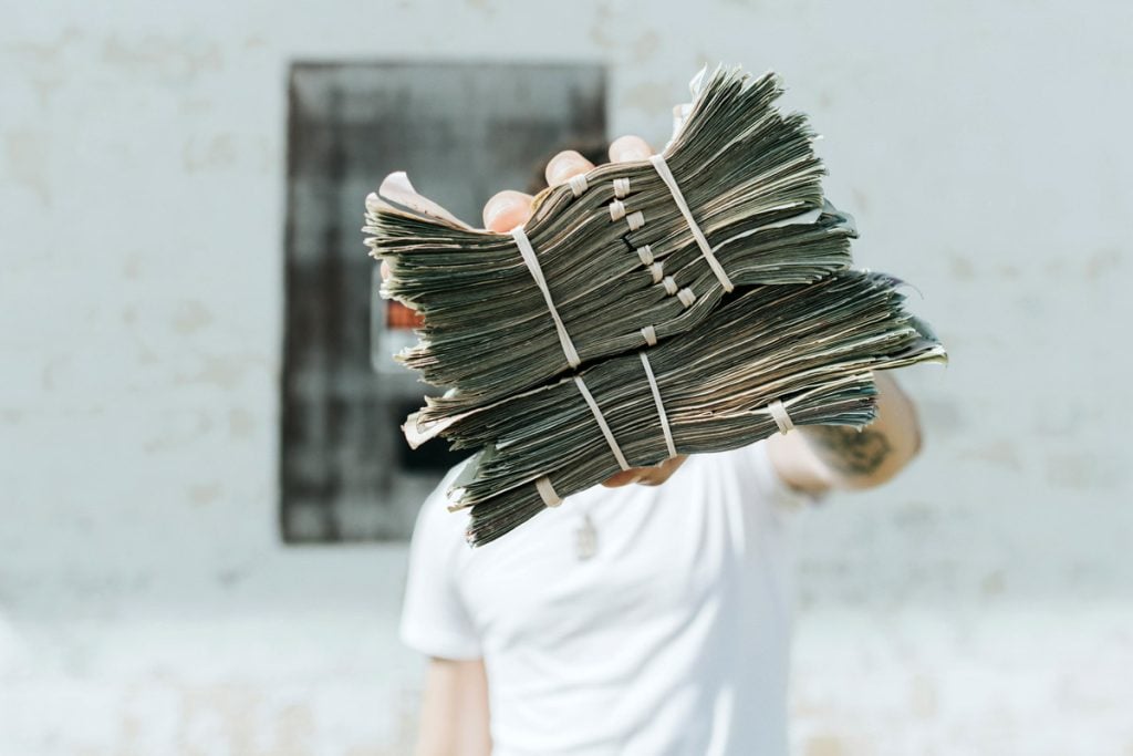 A man holds a few stacks of money bundled together with rubber bands. 