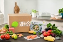 A Hello Fresh box sits on a kitchen counter with fresh food all around it and recipe cards.