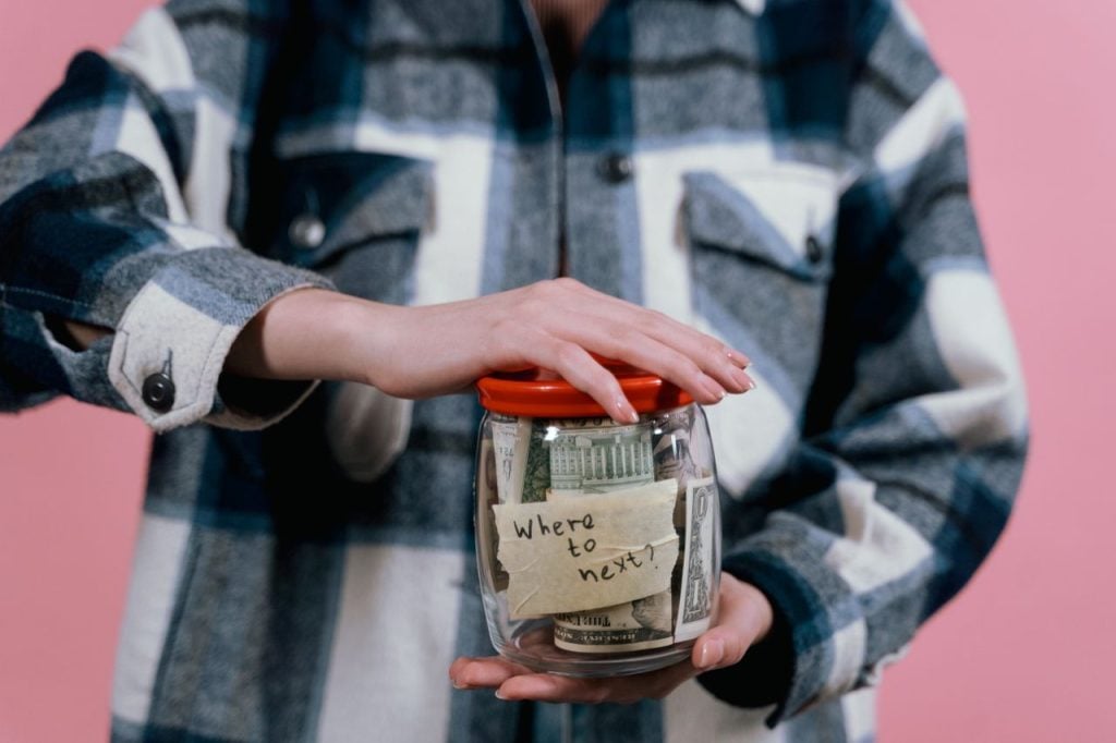 Person adding money to a labeled sinking fund jar toward a specific savings goal