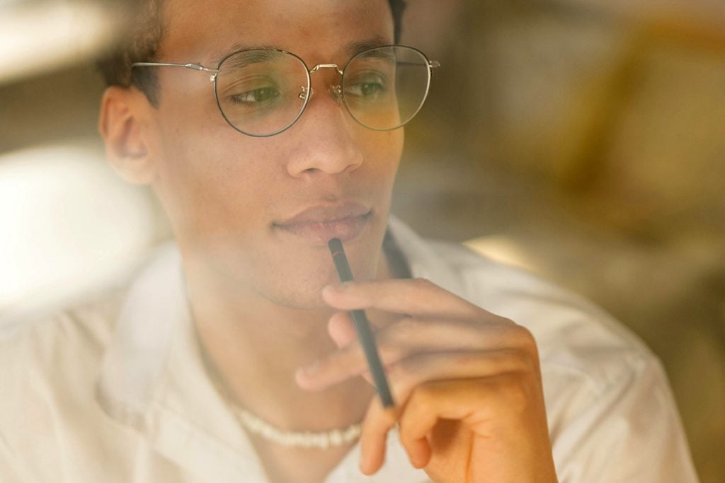 A man thinks about something with a pen up to his mouth.