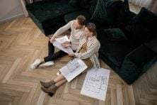 A man and woman sit on the floor while looking at home improvement plans.