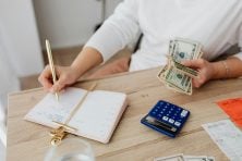 Someone holds money while using a notebook and calculator to budget.