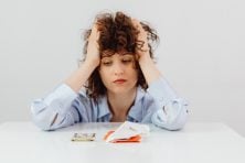 Woman has her hands in her hair as she looks at money and receipts.