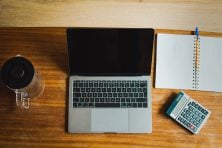 A laptop sits on a desk next to a calculator and a notebook.
